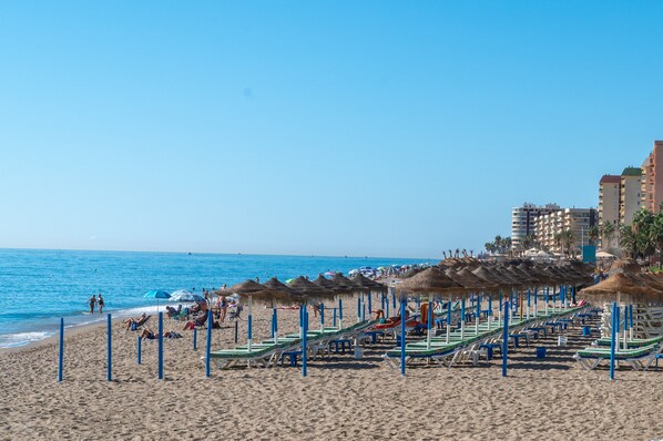 A beach with sun loungers, umbrellas, and a clear blue sky.