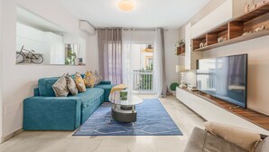Una sala moderna con un sofá color turquesa, una mesa de centro de vidrio, un televisor de pantalla plana y vistas a un balcón.