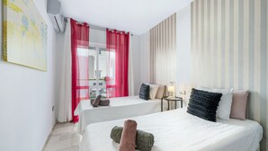Habitación de hotel con dos camas, una ventana con cortinas rojas, un aire acondicionado instalado en la pared y un papel tapiz a rayas.