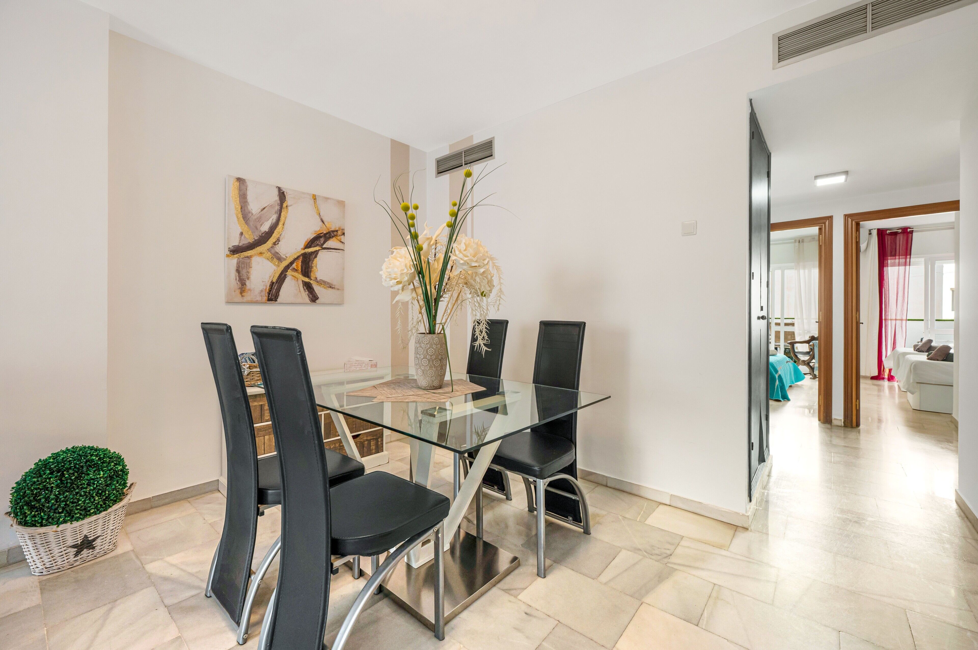 Un espace repas moderne avec une table en verre, des chaises noires, un vase de fleurs et un tableau accroché au mur.