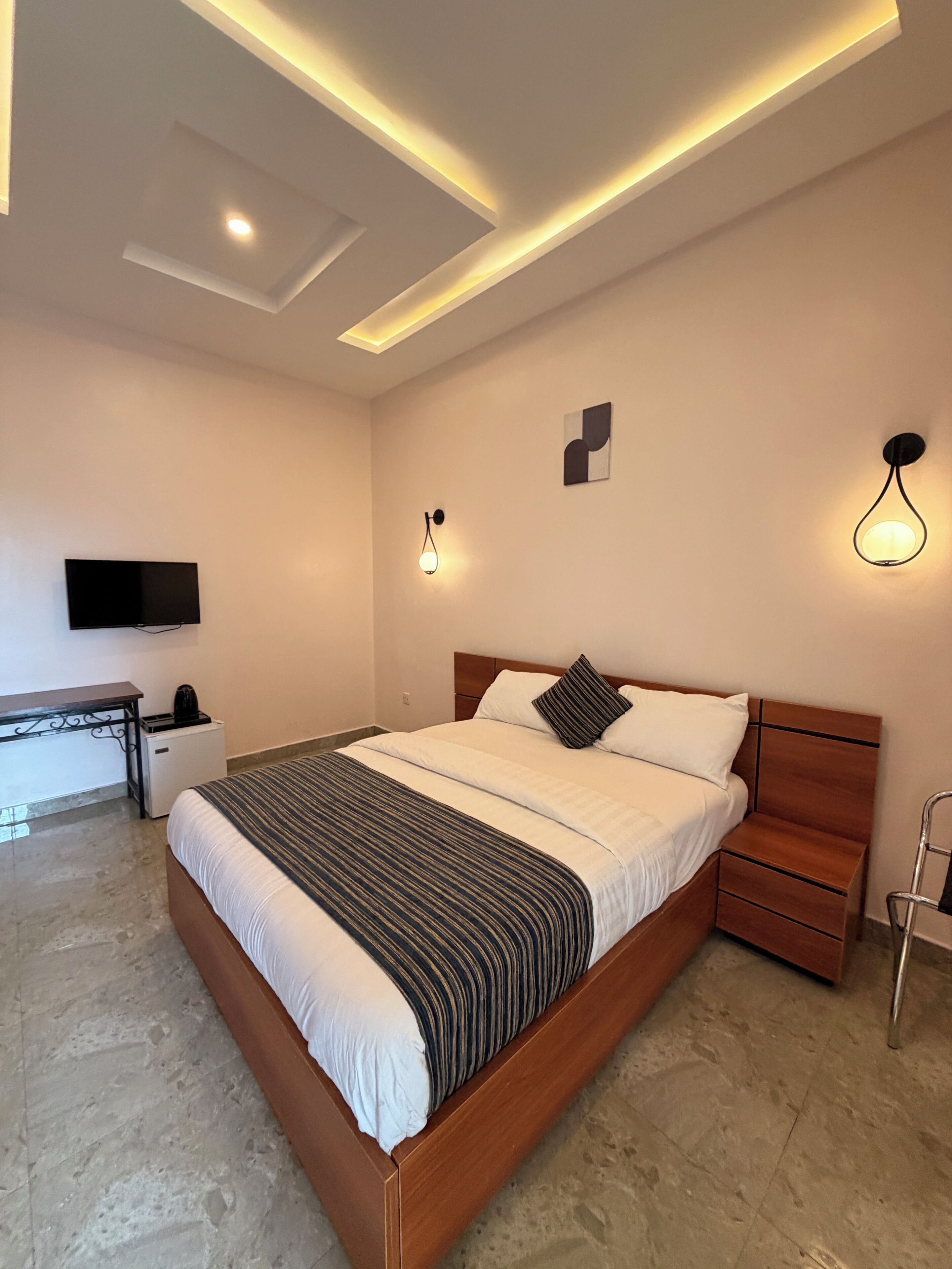 Een moderne hotelkamer met een groot bed, nachtkastjes, een flatscreen-tv en sfeervolle verlichting.