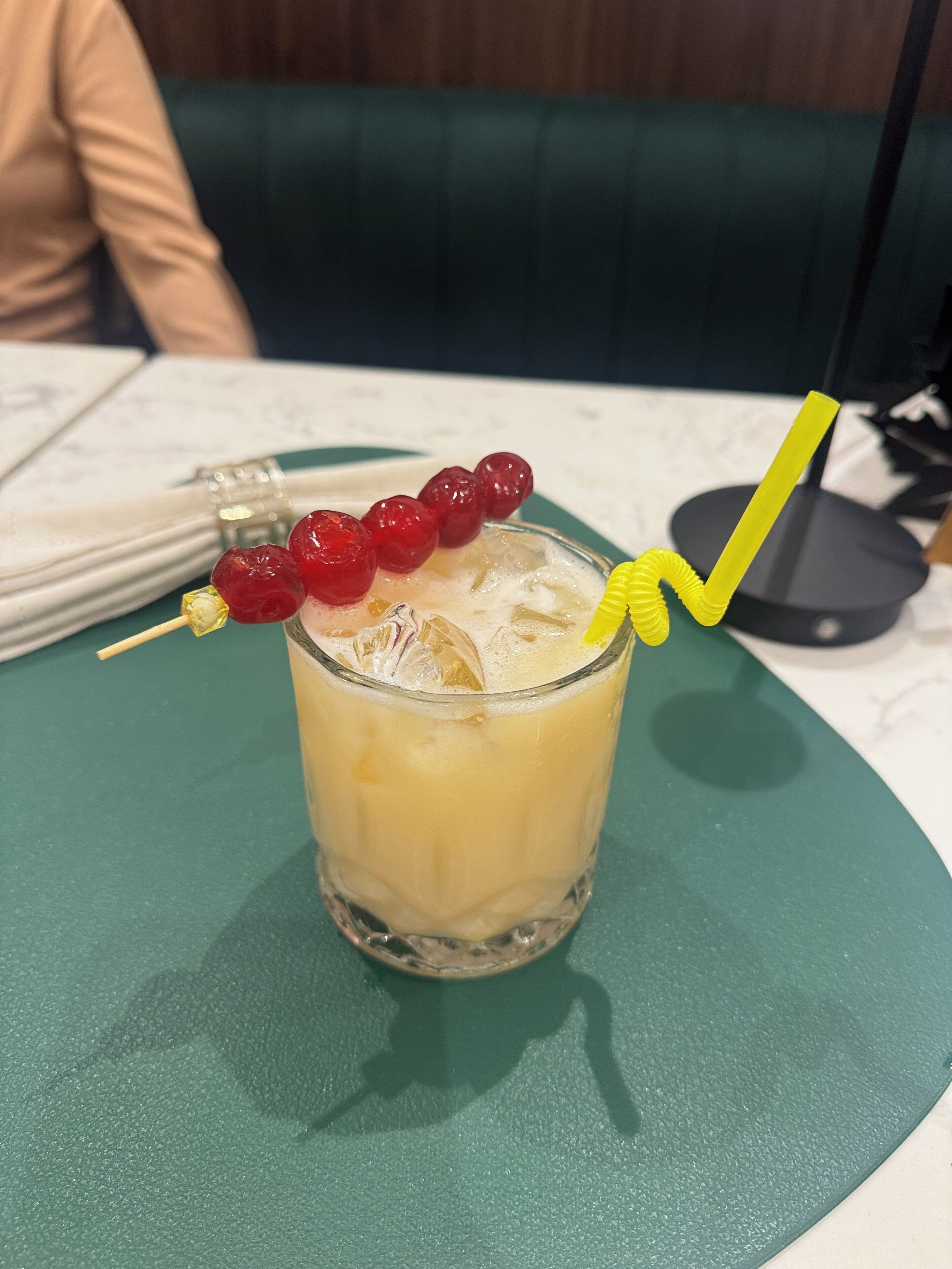 A glass with a yellow straw and red berries on a green tablecloth.