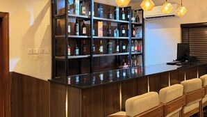 A bar area with wooden bar counter, multiple shelves with liquor bottles, and bar stools.