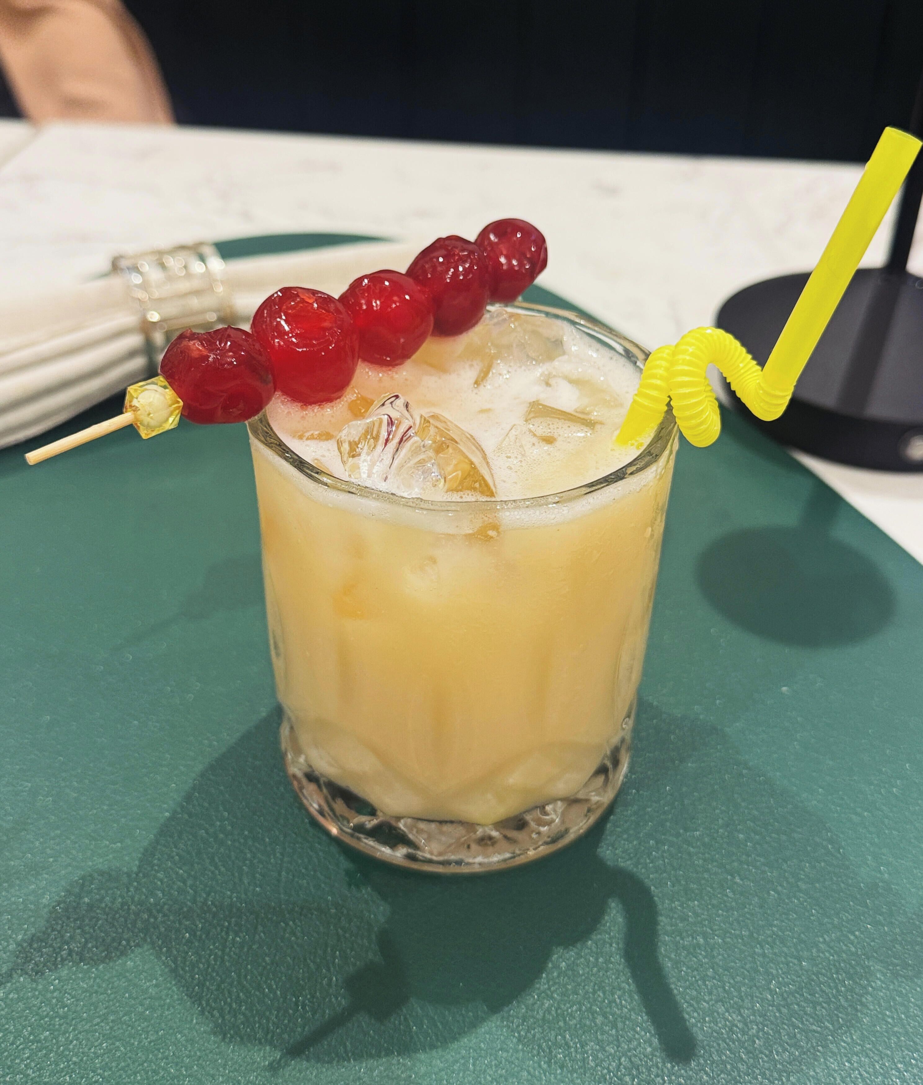 A glass with a yellow straw and red fruit garnish on a green tablecloth.