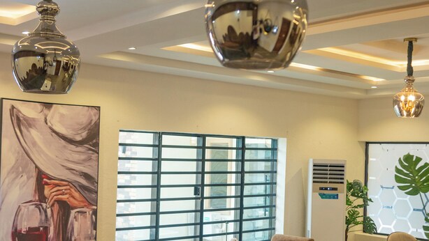 A modern restaurant interior with high ceilings, pendant lighting, and a large window with a grid pattern.