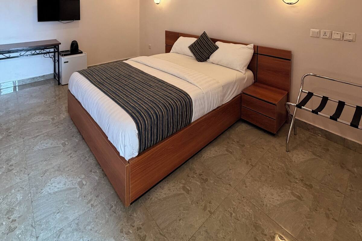 A modern bedroom with a wooden bed, bedside tables, a desk, and a TV mounted on the wall.
