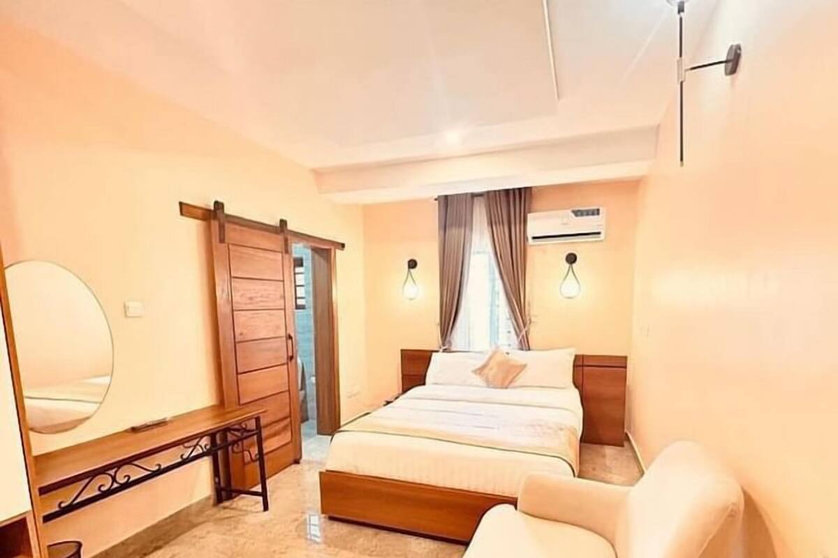 A bedroom with a bed, a chair, a mirror, and a wardrobe.