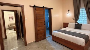 A bedroom with a bed, a sliding door, a wall-mounted light, and a view through a window.