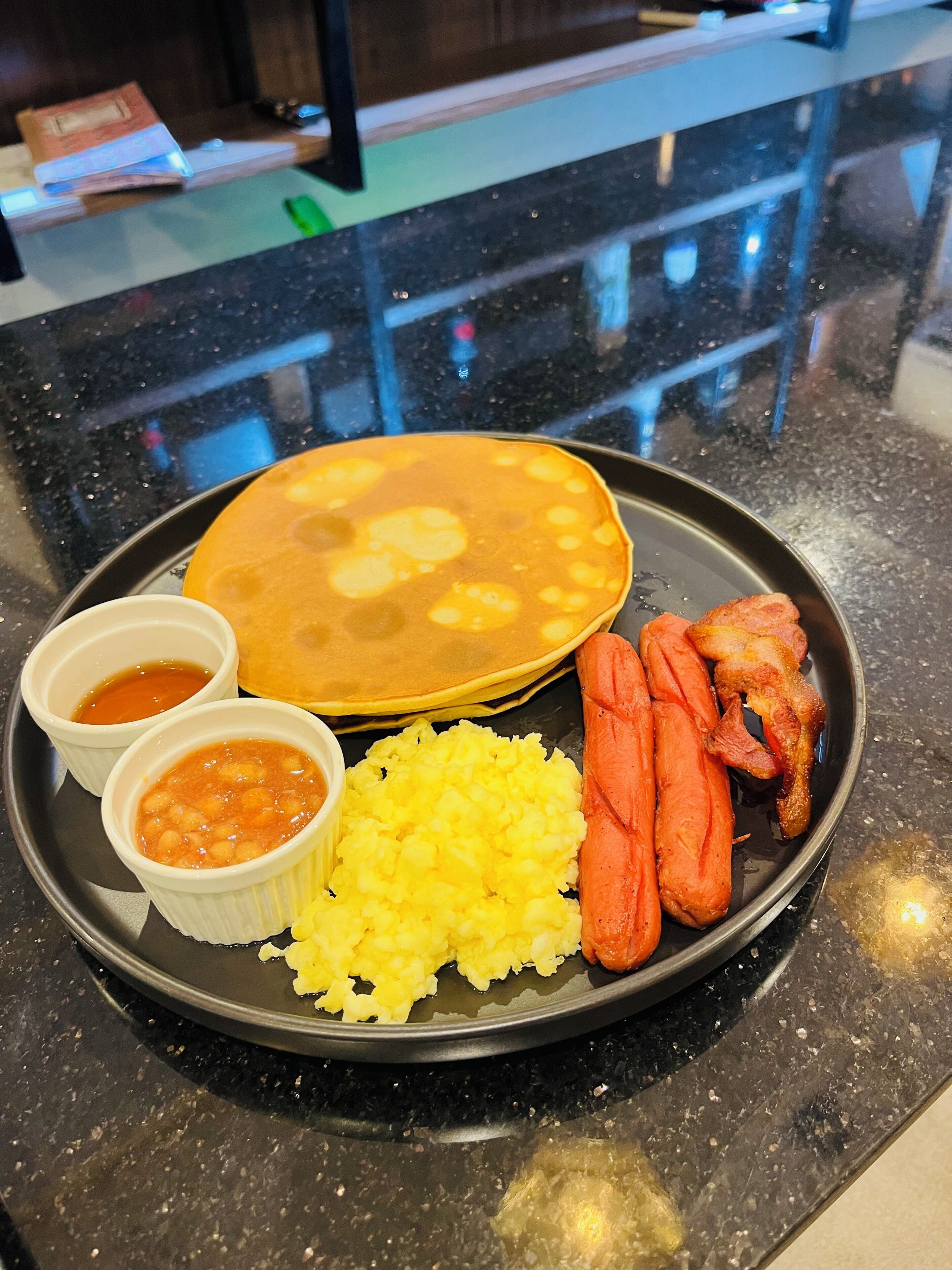 A plate with a soup, rice, and meat on a black countertop.