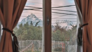 A view through curtains of a mountain landscape with a wooden fence and playground equipment.