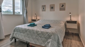 A bedroom with a bed, two bedside tables, a window with curtains, and wall art.