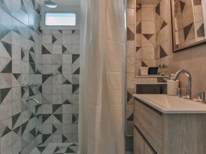 A modern bathroom with geometric patterned tiles, a shower area, a sink with a mirror, and a small shelf with toiletries.