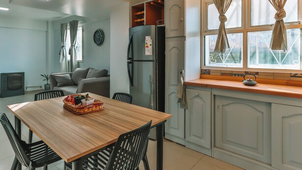 A modern kitchen with a wooden dining table, black chairs, a refrigerator, and a window with curtains.