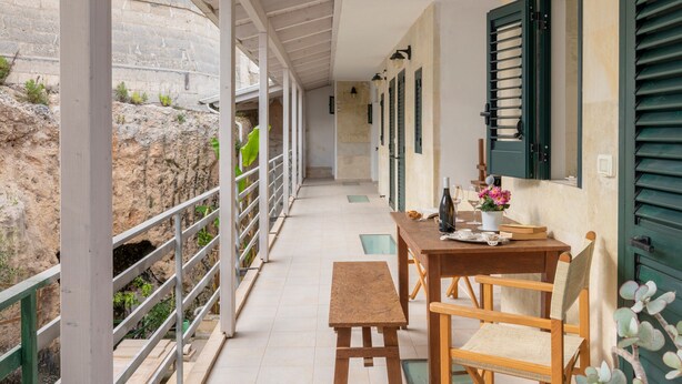 Un espacio al aire libre techado con una mesa, sillas, un banco y una barandilla con vistas a un paisaje rocoso.