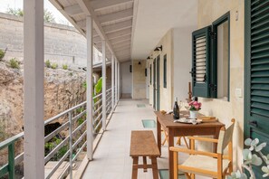 Un espacio al aire libre techado con una mesa, sillas, un banco y una barandilla con vistas a un paisaje rocoso.