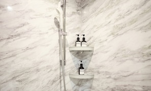 Un baño con piso de mármol y tres estantes blancos que contienen botellas de champú, acondicionador y jabón de baño.