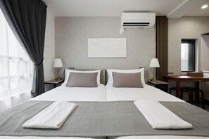 Una habitación de hotel con una cama grande, dos mesitas de noche, un escritorio y un equipo de aire acondicionado.