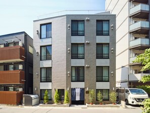 Un edificio moderno de varios pisos con balcones, ventanas amplias y un estacionamiento.