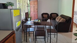 A compact kitchen with a refrigerator, a dining table with chairs, and a sofa.
