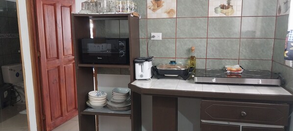 A compact kitchen with a microwave, toaster, and a small sink. There are stacked plates and a bottle on the counter. - Alan's House (Santa Elena)