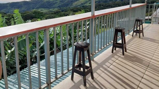 A covered outdoor area with a view of rolling hills, a railing, and two stools.