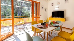 A dining area with a table set for two, yellow chairs, and a television mounted on the wall. - Sea Pine Retreat Apartment with Balcony, Wi-Fi, and Air Conditioning (Sorso)