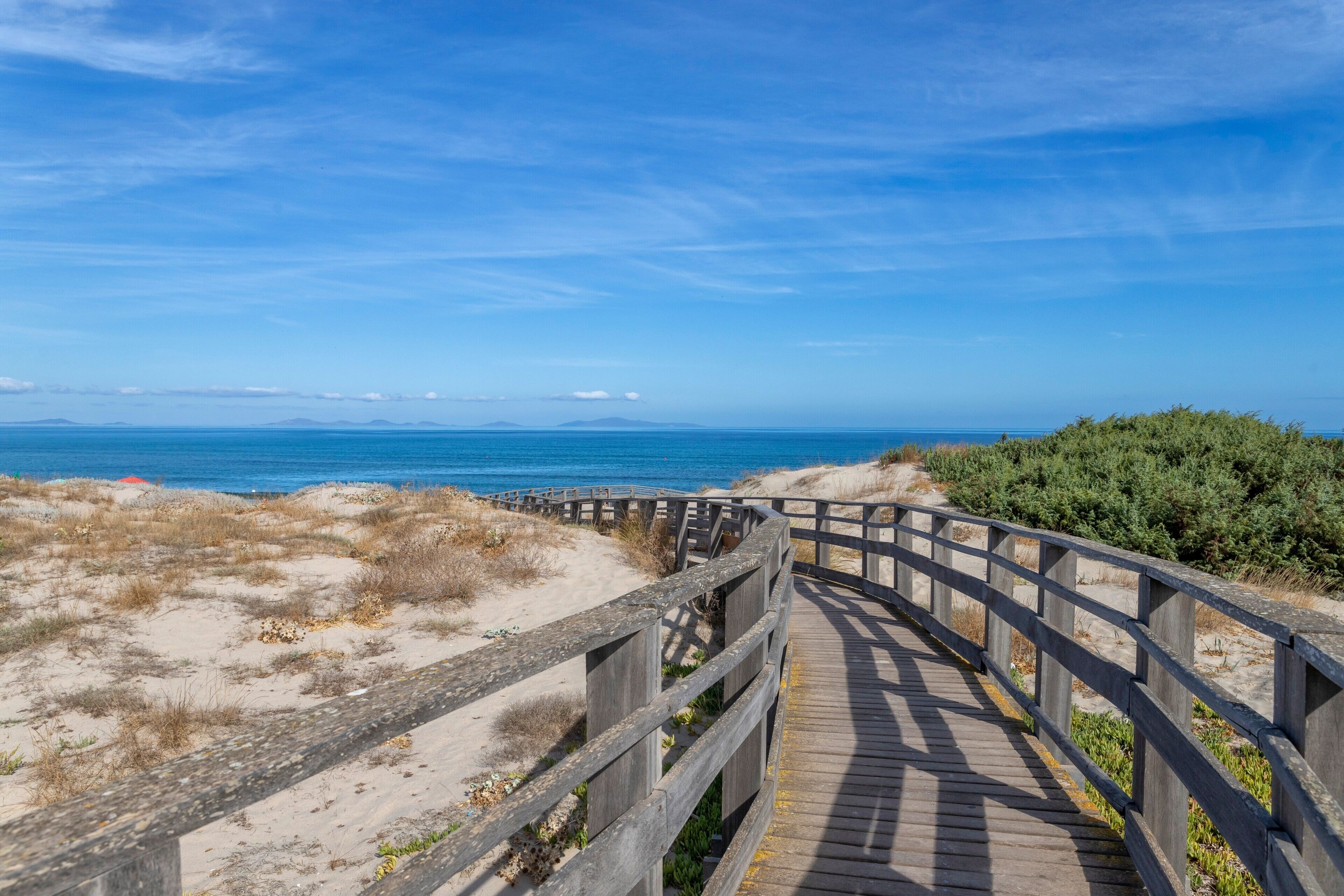 A wooden boardwalk leading to a beach with dunes and a clear blue sky.