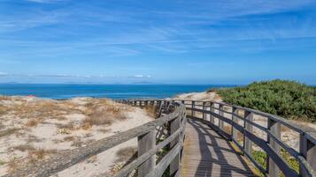 A wooden boardwalk leading to a beach with dunes and a clear blue sky.