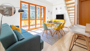 A modern living room with a sofa, a dining table with chairs, a TV, and a staircase. - Sea Pine Retreat Apartment with Balcony, Wi-Fi, and Air Conditioning (Sorso)