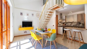 A modern kitchen with a dining area, a staircase, and a TV mounted on the wall. - Sea Pine Retreat Apartment with Balcony, Wi-Fi, and Air Conditioning (Sorso)