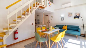 A dining area with a table, chairs, a staircase, a sofa, and a fire extinguisher. - Sea Pine Retreat Apartment with Balcony, Wi-Fi, and Air Conditioning (Sorso)