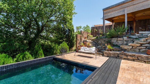 Une piscine dotée d’une terrasse en bois, de murs en pierre et de mobilier d’extérieur.