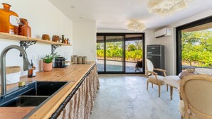 Une cuisine moderne avec un plan de travail en bois, un évier et une vue sur un vignoble, visible à travers de grandes portes vitrées.