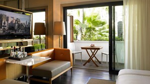 Ein Hotelzimmer mit einer Couch, einem kleinen Tisch, einem Fernseher und einem Balkon mit Pflanzen.