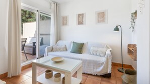 Ein Zimmer mit einem weißen Sofa, einem Glastisch, einer Stehlampe und Blick durch eine Schiebetür.