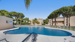Ein Swimmingpool mit weißem Zaun, Palmen und Apartmentgebäuden im Hintergrund.