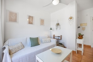 Een witte kamer met een bank, een tafel en decoraties aan de muur, waaronder ingelijste bladeren en droomvangers.