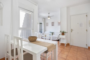 Een witte eetruimte met een tafel, stoelen en een plafondventilator.