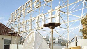 Un espacio exterior moderno con una mesa de vidrio, una silla blanca acolchada y una lámpara de pie.