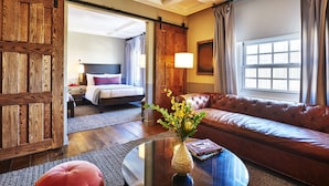 Hotelkamer met een groot raam, een leren bank, een houten deur en een glazen salontafel met een vaas.