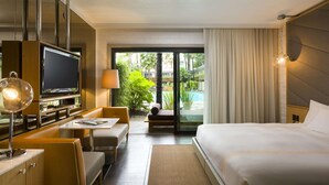 Una camera d'albergo con un letto, una televisione, una scrivania e vista su una piscina e sulla vegetazione.