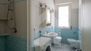 A compact bathroom with a shower, toilet, sink, and washing machine. - Homiday - Via Gramsci, Azure Two-Bedroom Apartment (Pineto)