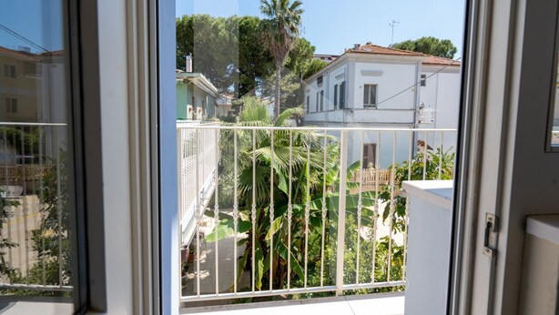 A balcony with a metal railing, overlooking a residential area with houses and palm trees. - Homiday - Via Gramsci, Azure Two-Bedroom Apartment (Pineto)