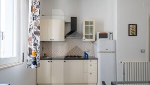 A compact kitchen with light-colored cabinets, a gas stove, a microwave, and a small refrigerator. - Homiday - Via Gramsci, Azure Two-Bedroom Apartment (Pineto)