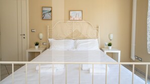 A bedroom with a white metal bed frame, two bedside tables with lamps, and a door to the left. - Homiday - Via Gramsci, Azure Two-Bedroom Apartment (Pineto)