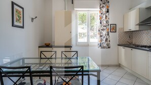 A modern kitchen with white cabinets, a glass dining table, and a view through the open door. - Homiday - Via Gramsci, Azure Two-Bedroom Apartment (Pineto)