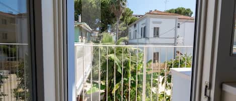 En balkon med gelænder i metal, der giver udsigt over et boligområde med huse og palmer.