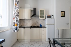 A compact kitchen with light-colored cabinets, a gas stove, a microwave, and a small refrigerator.