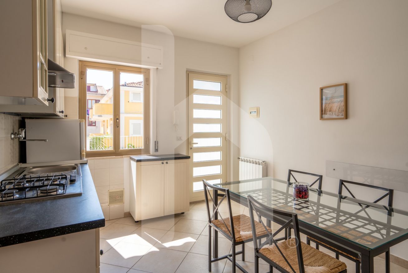 A kitchen with a gas stove, a sink, and a window. There is a dining table with chairs and a glass top.