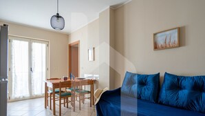 Ein Wohnzimmer mit blauem Sofa, einem Esstisch mit Stühlen und einer Hängelampe.
